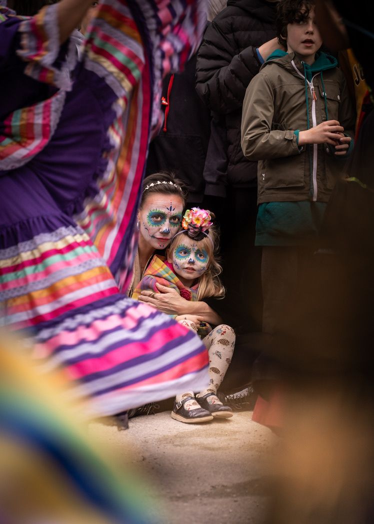An adult and child with colourful face paint watch a performance behind a swirling striped skirt.